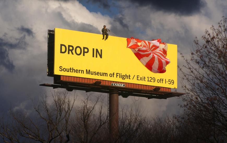 南部航空博物館の屋外広告。看板の上にいるのはパラシュートで降り立ったパイロットのようです。家族連れに強くアピールしそうです。＜米国＞