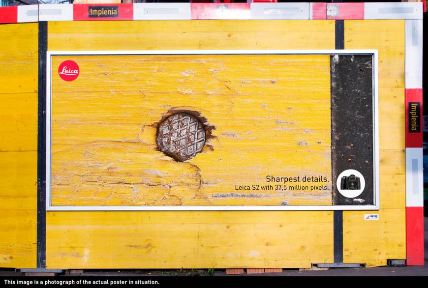 カメラ（ライカ）の屋外広告。黄色い壁に打たれた釘のズームアップ写真、その鮮明さが表現されているようです。＜スイス＞